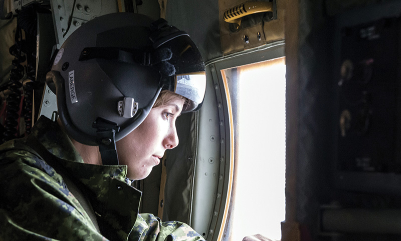 Un membre féminin de l’équipage regarde par le hublot d’un avion CC-130J Hercules.