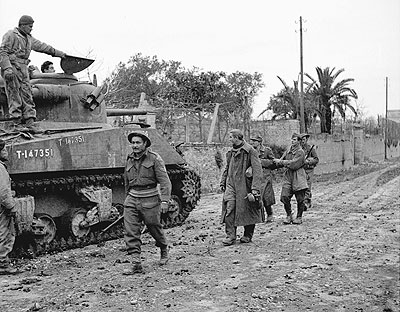 Captured German paratroopers passing a Sherman tank