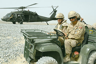 Soldiers in Jeep with helicopter in background.