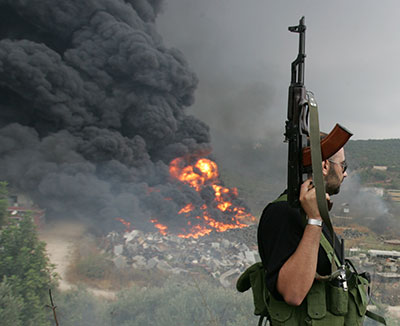 A Lebanese Hezbollah guerrilla observes a fire rising from a burning object in a Beirut suburb, 17 July 2006.