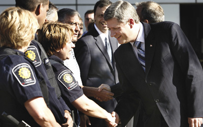 Stephen Harper, premier ministre du Canada, salue des gardes-frontière canadiens, à son arrivée au poste frontalier canado-américain de Cloverdale, le 31 août 2006. Il venait juste d’annoncer qu’à partir de septembre 2007, les gardes frontière canadiens seraient armés, comme leurs homologues américains.