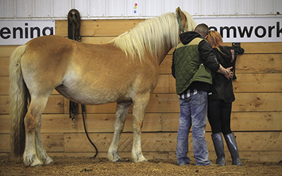 (Veteran/fiancee embrace near horse)