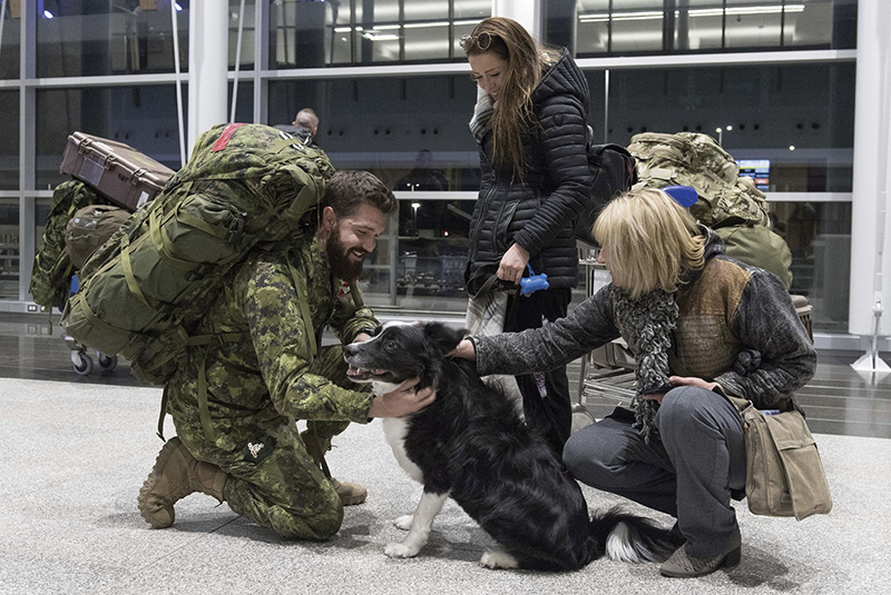 Soldier returning from overseas deployment being greeted by family, including the family dog.